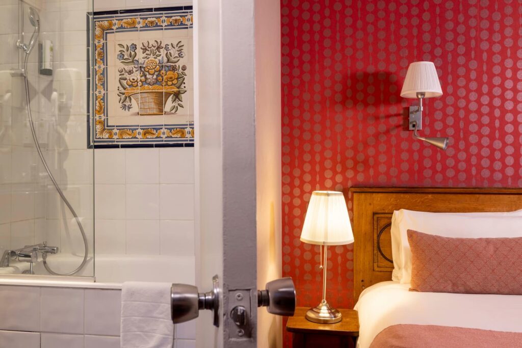 chambre avec tissu rouge, lampe, lit avec oreiller rose et salle de bain avec baignoire et faience au Welcome Hôtel paris - hotel salon international de la lingerie paris