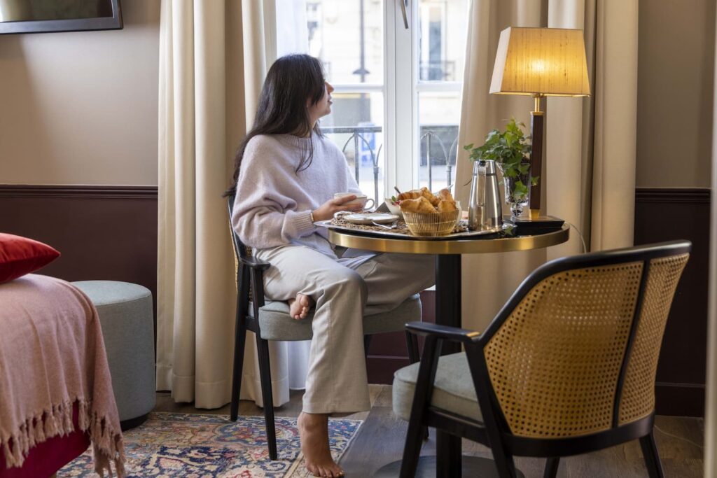 Cliente prenant le petit-déjeuner dans sa chambre devant la fenêtre du Welcome Hôtel Paris - Hiver à Paris