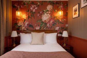 chambre single supérieure paris : lit double avec un coussin, tissu rouge fleuri, deux appliques allumées et deux lampes blanches - WELCOME HOTEL paris