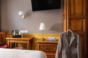 hotel chambre double paris - armoire avec veste de costume pendue à la poignée, commode en bois, bureau en bois avec plateau de courtoisie, lampe et télévision
