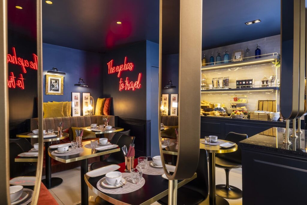 Salle du petit-déjeuner, murs bleus, néon rouge, tables dressées. Lieu instagrammable Paris - Welcome Hotel Paris